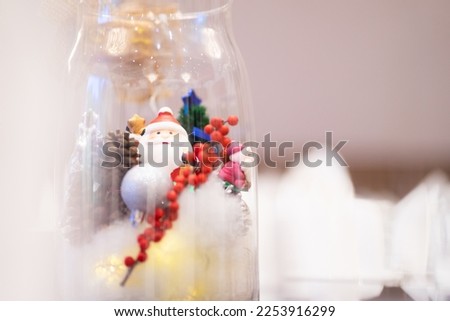 Santa Claus doll with a Christmas tree in a glass jar under soft light.