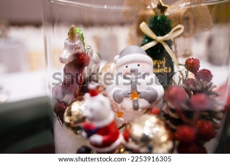 A white snowman with a Christmas tree and a unicorn in a glass jar under soft light.