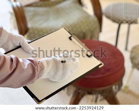 Gloved hand holding a clipboard in front of many chairs Royalty-Free Stock Photo #2253924129