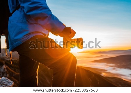 A male photographer taking a photo on the mountain top at sunrise or sunset adventure travel photography. 