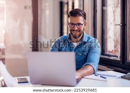Smiling businessman sitting in office and working on laptop. Royalty-Free Stock Photo #2253929681