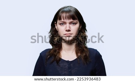 Headshot portrait of young female looking at camera on light background