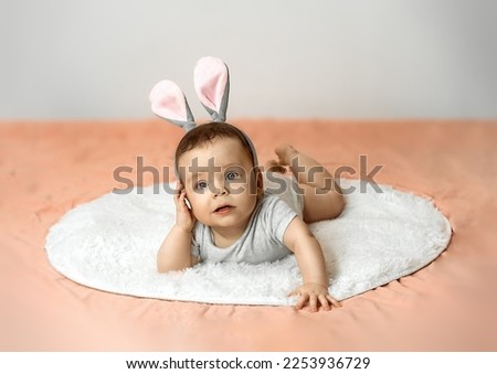 A surprised newborn baby is lying on the bed, wearing bunny ears on Easter morning. Copy space. High quality photo