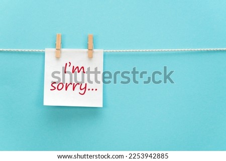 White reminder paper on a rope with a clothespin with a motivational inscription I'm sorry in handwritten font on a colored background with free space for text