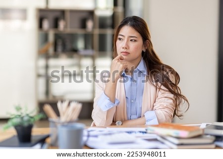 Image of young beautiful brooding Asian woman working with laptop while sitting at laptop in office, thinking of professional plan, project management, considering new business ideas. Royalty-Free Stock Photo #2253948011