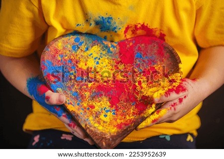 children's hands hold a wooden plate in the shape of a heart in which the multi-colored bright colors of Holi. Indian festival of colors Holi.