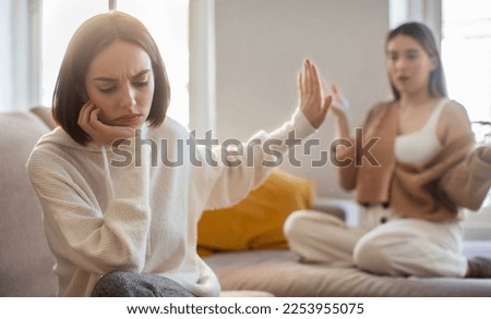 Offended sad european millennial lady ignores screaming displeased girlfriend, making stop sign with hand in living room interior. Scandal, quarrel and relationship problems at home, people emotions Royalty-Free Stock Photo #2253955075