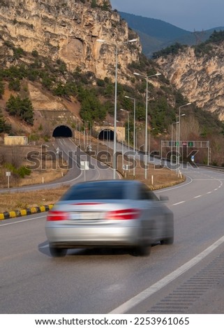 Car with motion blur driving on highway towards tunnel under hill.