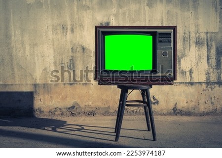 Vintage TV set on a chair with green screen in front of old wall background.