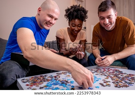 Friends playing jigsaw puzzles at home, on a white wooden table. Putting things together and solving problems. Diversity and fun in a friendship. Royalty-Free Stock Photo #2253978343