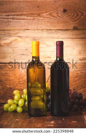 Red and white wine bottle with grapes and barrel on wooden rustic table.