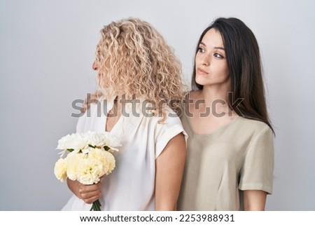 Mother and daughter holding bouquet of white flowers looking to side, relax profile pose with natural face and confident smile. 