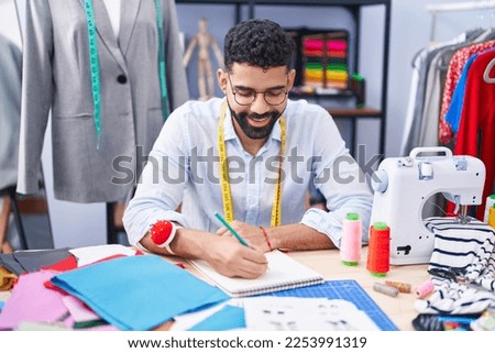 Young arab man tailor smiling confident drawing on notebook at tailor shop
