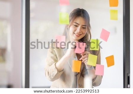share idea, project successful, Business Asian business woman in meeting brainstorming and use post paper and writing note and stick on glass wall at workplace office. Royalty-Free Stock Photo #2253992513