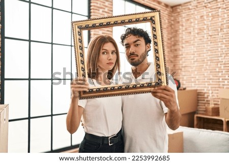 Young two people holding empty frame together skeptic and nervous, frowning upset because of problem. negative person. 