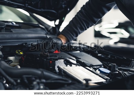 Close-up shot of unrecognisable man wearing black glove inspecting car engine and interior of hood of car. Garage work. Horizontal indoor shot. High quality photo Royalty-Free Stock Photo #2253993271