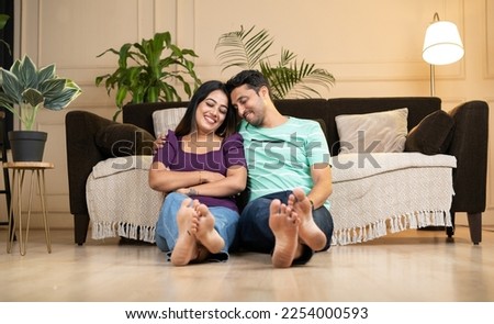 wide shot of happy smiling indian couple embracing each other by eyes closed at home while sitting on floor - concept caring husband, newly married couples and relationship bonding Royalty-Free Stock Photo #2254000593