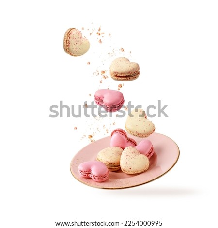 French sweet colorful heart shape cookies macarons macaroons with crumbs flying falling on vintage pink plate isolated on white background. Pastry shop card with copy space. Valentines day. Royalty-Free Stock Photo #2254000995
