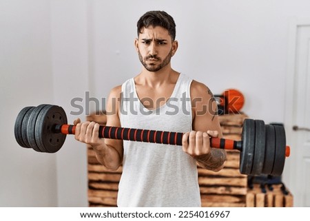 Young hispanic man training with weighs skeptic and nervous, frowning upset because of problem. negative person. 