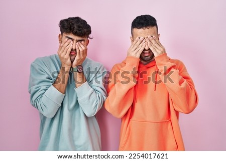 Young hispanic gay couple standing over pink background rubbing eyes for fatigue and headache, sleepy and tired expression. vision problem 