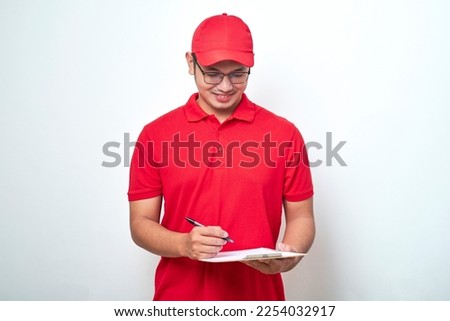 Young smiling asian delivery man in red uniform and cap holding clip board, write down customer order standing on isolated white background. Royalty-Free Stock Photo #2254032917