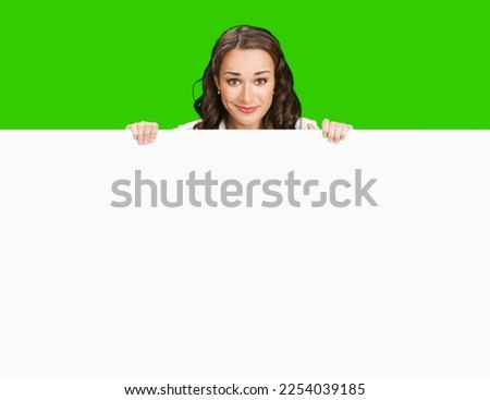 Smiling business woman standing beehind, peeping out white empty mock up signboard. Success and advertising concept. Copy space place. Young businesswoman. Green chroma key background.