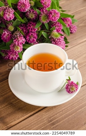 Healthy herbal tea with clover in a white cup on a brown wooden background with a bouquet of clover.