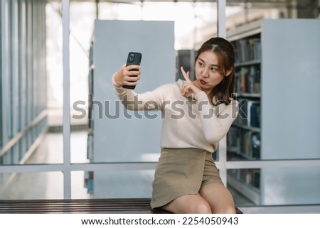 Pretty Asian woman student using smartphone for video call, line chat, taking photos and doing various task via online application.