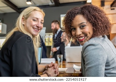 Young black south american woman looking at camera with her blonde caucasian colleague while working in modern office - Break from work and coworking concept Royalty-Free Stock Photo #2254051927