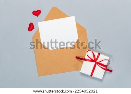 Above view St. Valentines day flat lay composition with craft paper envelope and blank white card to write best wishes, isolated on grey background. Mock up, copy space for your design.