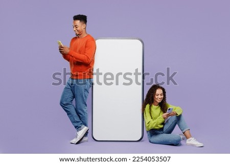 Full body young couple two friends family man woman wear casual clothes together sit big huge blank screen mobile cell phone with area use smartphone isolated on pastel plain light purple background