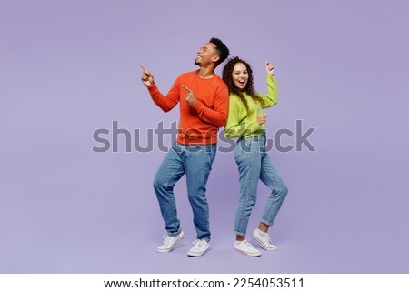 Full body sideways fun young couple two friends family man woman of African American ethnicity wear casual clothes together point finger aside on area isolated on pastel plain light purple background