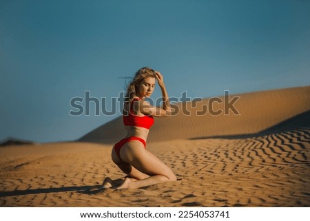 Red Bikini Woman Kneeling on Sand Dunes Royalty-Free Stock Photo #2254053741