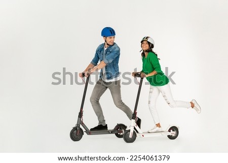 pretty stylish couple riding on electic kick scooter isolated on white studio background summer hipster style having fun together smiling happy, driving on speed wearing safety helmets Royalty-Free Stock Photo #2254061379