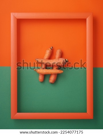 Hashtag symbol from carrots in wooden picture frame on orange and green background