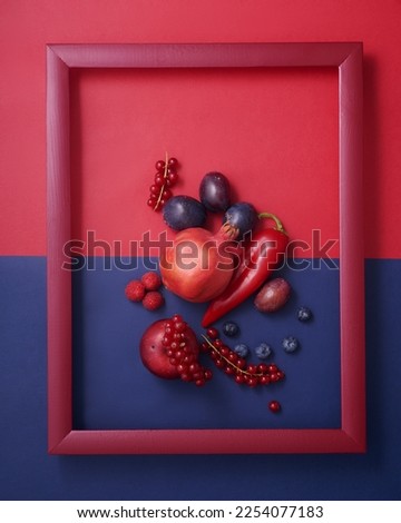 Apple, plum, pepper, pomegranate, blueberry, raspberry, and currant in wooden picture frame on red and blue background