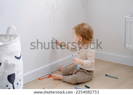 Toddler scribbling on white wall at home. Little kid drawing on walls by colored markers. Art therapy, normal development.  Royalty-Free Stock Photo #2254082751