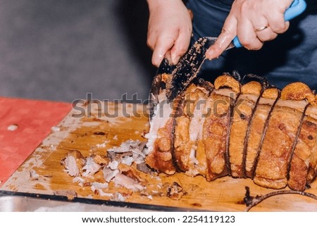 Traditional Italian dish of pork porchetta, fresh from the oven. The chef cuts into pieces an Italian meat delicacy