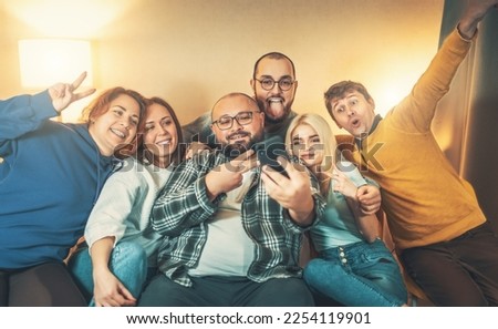 Friends at home party taking selfie, laughing, having good time. Use phone for video calling remotely and for taking diversity selfie photo