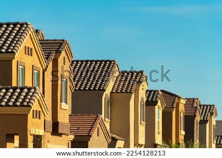 Row of suburban neighborhood with visible windows and adobe style roofs and orange and beige stucco facades. In late afternoon sun with copy space blue sky background in downtown urban city. Royalty-Free Stock Photo #2254128213