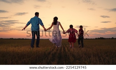 Parental care for children. Active family with children runs through a grassy field in the evening at sunset. Big family, group of people in nature. Son, Daughter, dad, mom, walk hand in hand outdoors