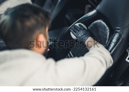 Rear view of man wearing black gloves waterproofing car seat leather upholstery. Protective coating. Professional car detailing process. Blurrred background. Horizontal indoor shot. High quality photo