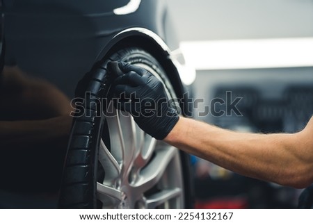 Close-up shot of unrecognisable man wearing black glove blackening tires of car using sponge. Professional car detailing in a garage. Horizontal indoor shot. High quality photo