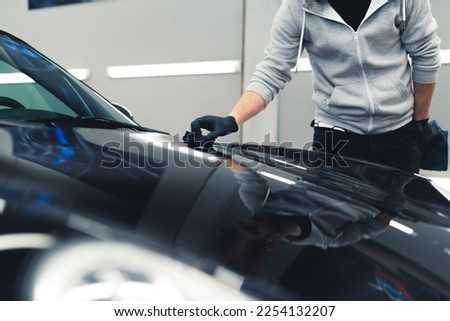 Man wearing black gloves applying ceramic coating to front of black car using sponge. Professional car detailing process. Horizontal indoor shot . High quality photo