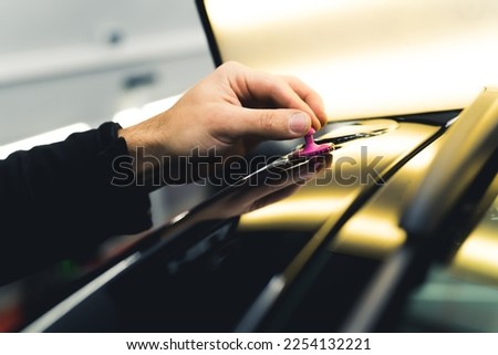 Close-up shot of unrecognisable man hand removing small dent in car using bright lamp in a garage. Professional car repair and detailing. Horizontal indoor shot. High quality photo