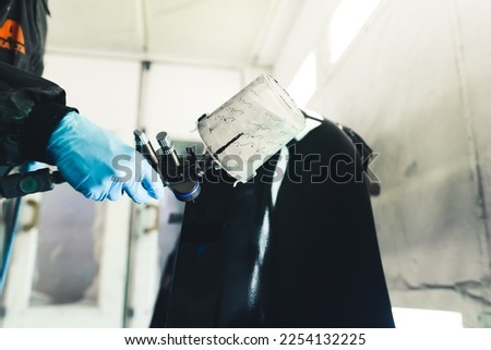Person wearing protective uniform and gloves holding airbrush painting part of car black. Car paintwork. Horizontal indoor shot . High quality photo