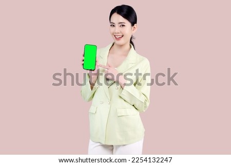 Pretty Asian woman show blank green screen of mobile telephone and point finger isolated on pink background.