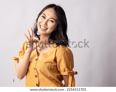 Portrait of young beautiful Indonesian Asian woman in casual shirt smiling while showing okay gesture isolated on white background studio portrait. Achievement career concept