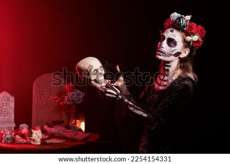 Santa muerte model helping skull with smartphone to speak on call, posing in studio on day of the dead holiday celebration. Looking like la cavalera catrina on mexican halloween festival.