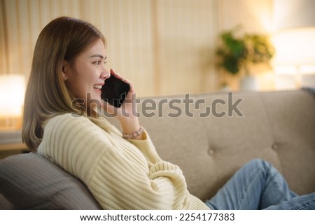 Happy asian woman using mobile phone and receiving good news
on sofa at living room